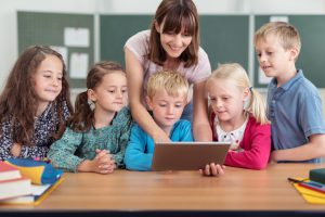 Grundschüler gespannt mit Lehrerin vor Laptop